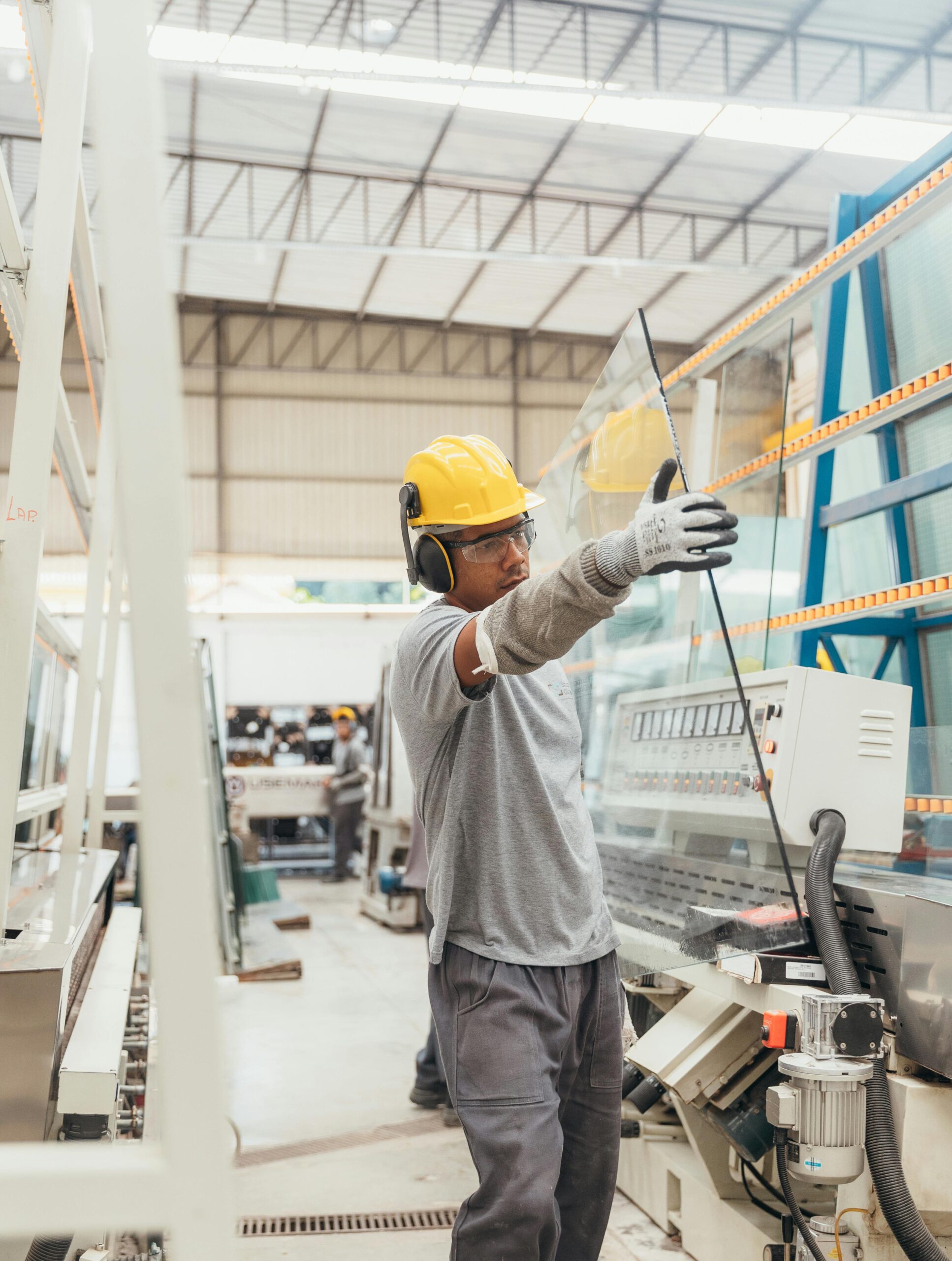 Industrial worker with safety gear handling glass sheet in a factory environment.